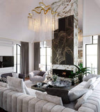 Seen from below, this lit gold Clérachic chandelier hangs in a living room with a patterned marble fireplace wall.