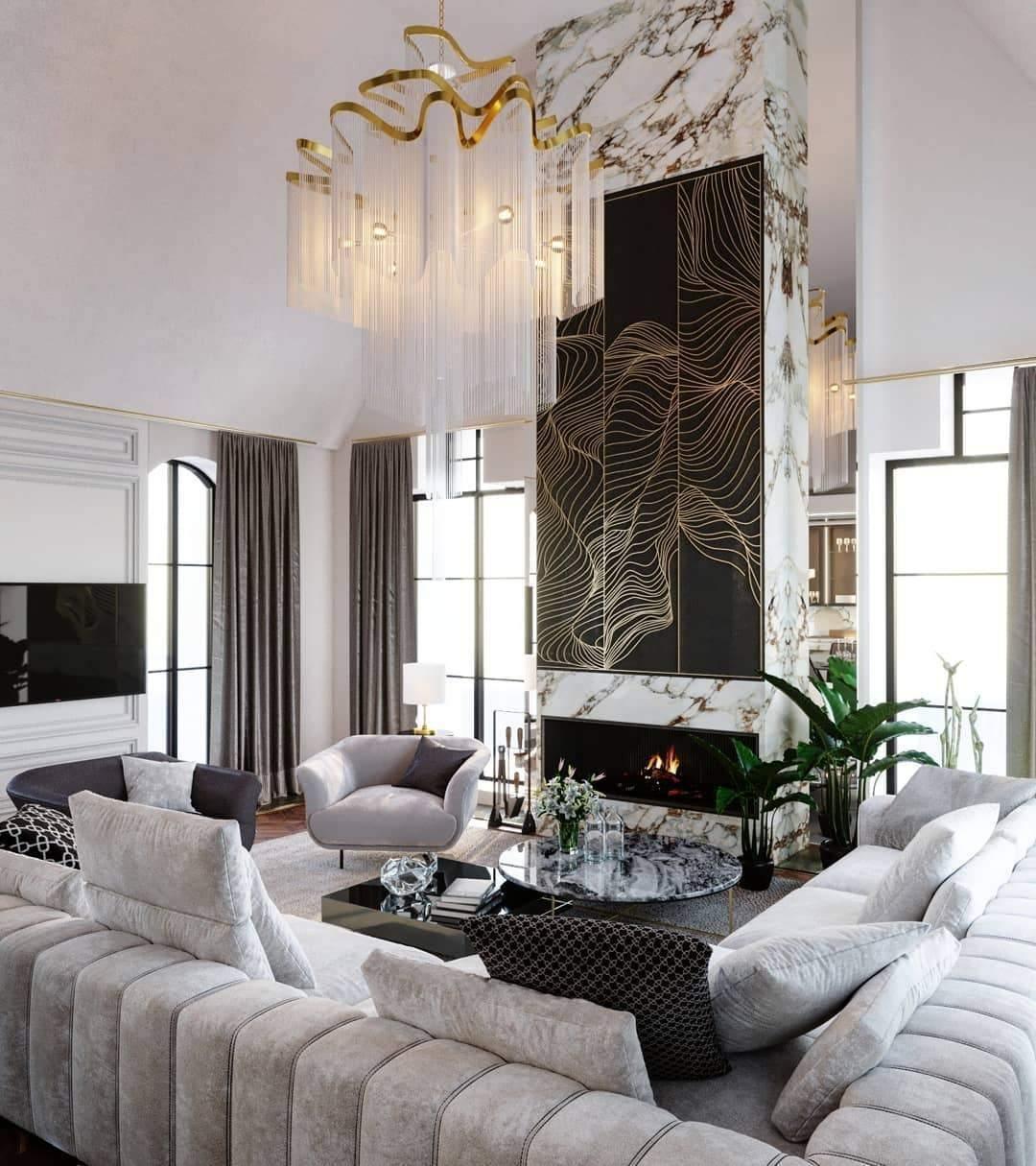 Seen from below, this lit gold Clérachic chandelier hangs in a living room with a patterned marble fireplace wall.