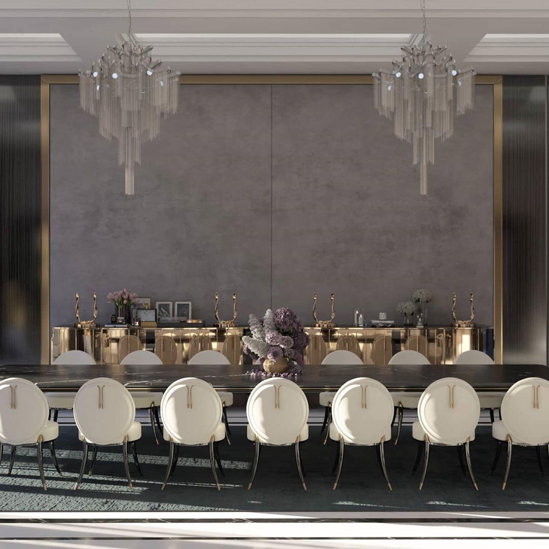 Two silver Clérachic chandeliers light a long dining table with cream upholstered chairs in a grand hall.