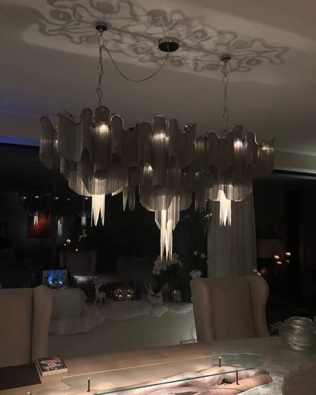 At night, this silver Clérachic chandelier glows in a dim lounge, its chain reflected in the dark windows.