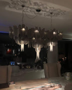 At night, this silver Clérachic chandelier glows in a dim lounge, its chain reflected in the dark windows.