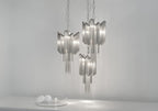 Three silver Clérachic chandeliers cluster together, lit, above small glass orbs on a plain backdrop.