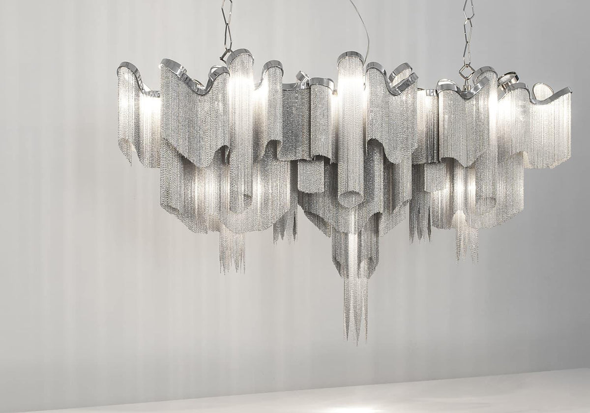 On a plain backdrop, this lit silver Clérachic chandelier is shown tiered with its chain catching the light.