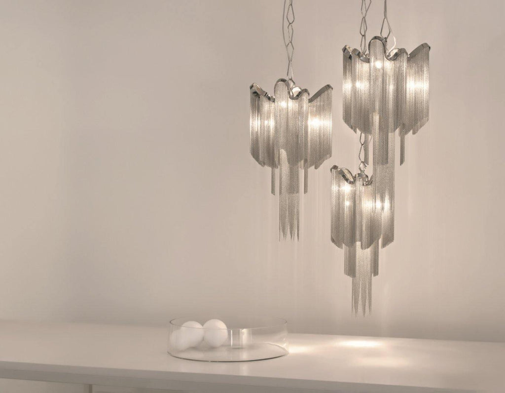 Two silver Clérachic chandeliers hang lit together against a plain backdrop, with glass orbs on the surface below.