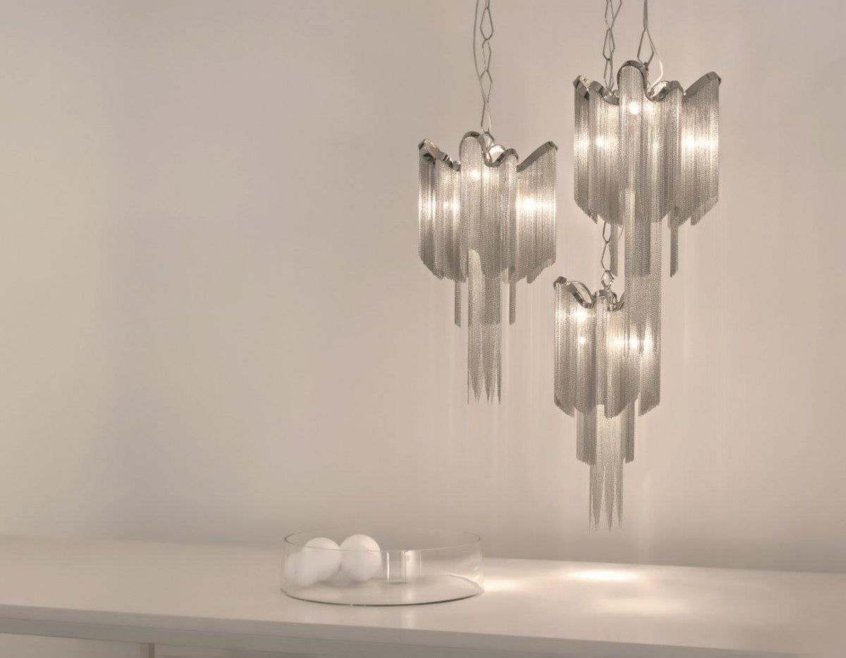 Two silver Clérachic chandeliers hang lit together against a plain backdrop, with glass orbs on the surface below.