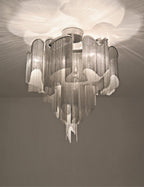 Backlit dramatically, this silver Clérachic chandelier's tiers glow bright against a hazy pale backdrop.