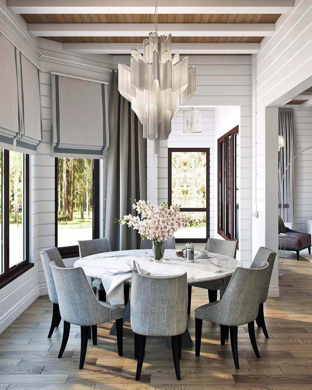 Beneath a wood-beamed ceiling, this lit silver Clérachic chandelier hangs above a round table and wicker chairs.