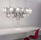 Stretching wide above a long white dining table, this lit silver Clérachic chandelier hangs beside a red chair.