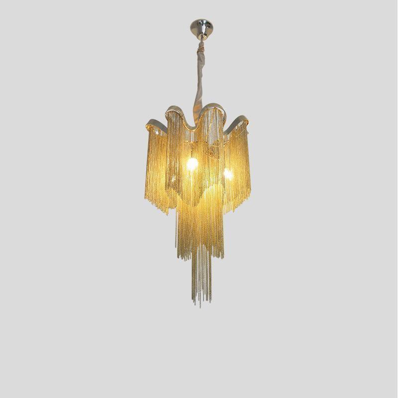 A gold Clérachic chandelier, lit, is shown tiered against a plain grey backdrop.