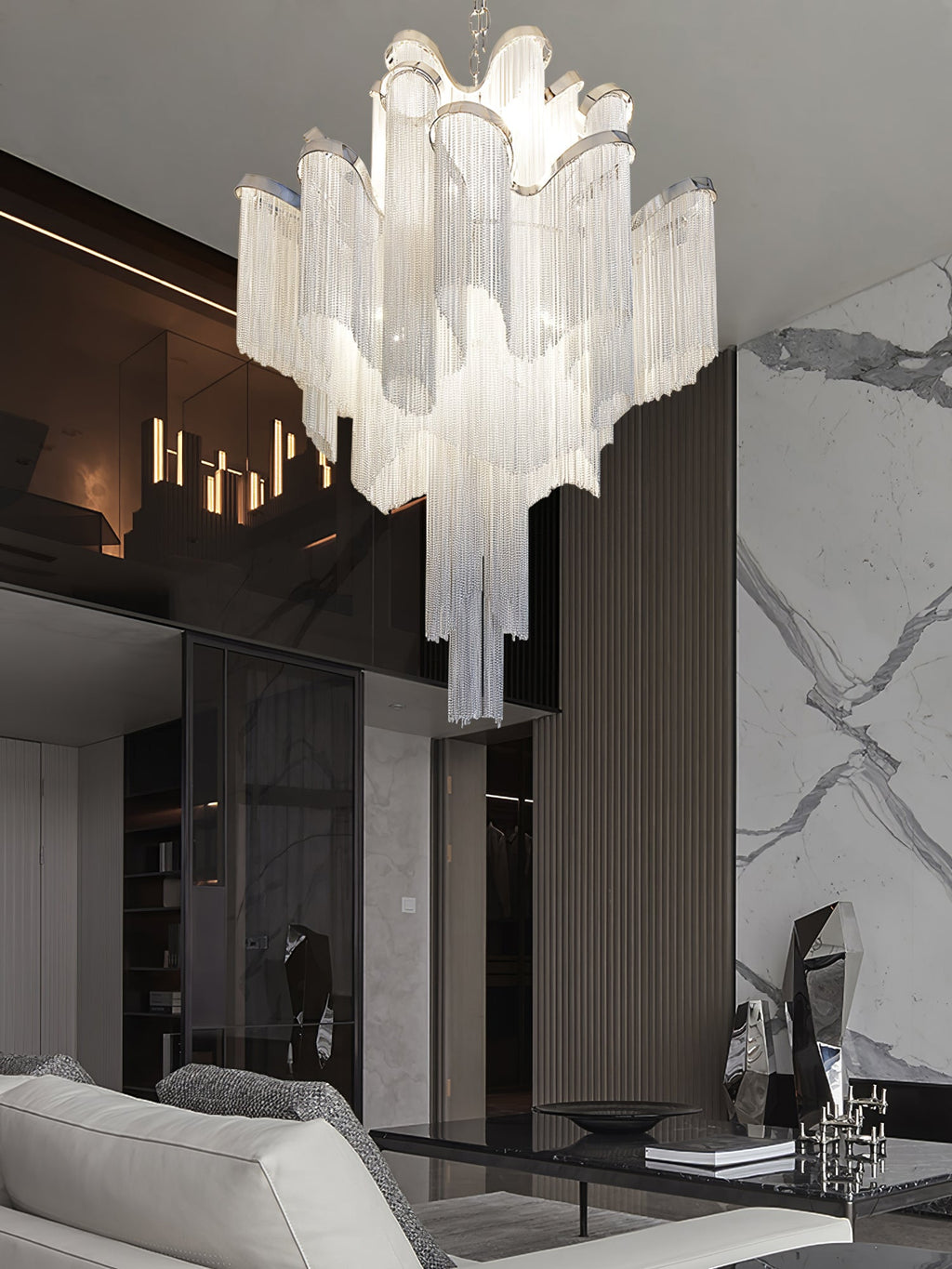 A marble wall and lit candle sconces frame this lit silver Clérachic chandelier in a modern living room.
