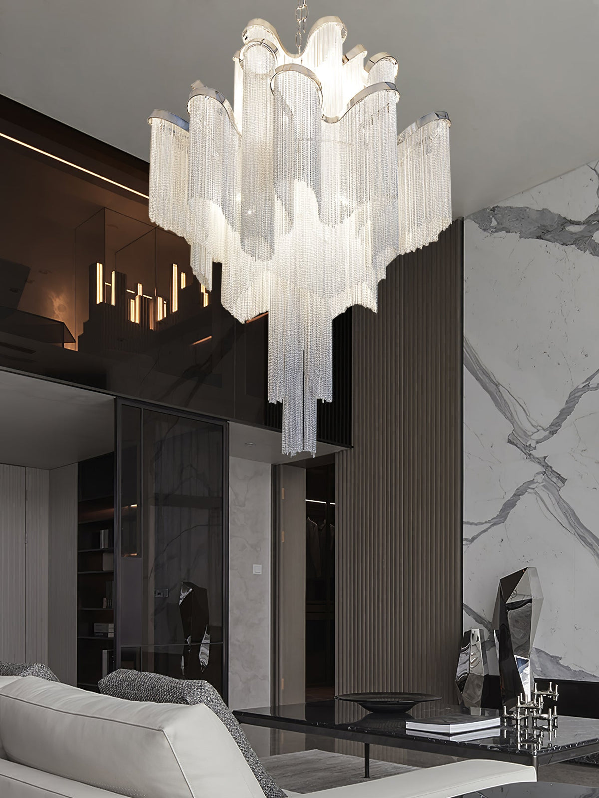 A marble wall and lit candle sconces frame this lit silver Clérachic chandelier in a modern living room.