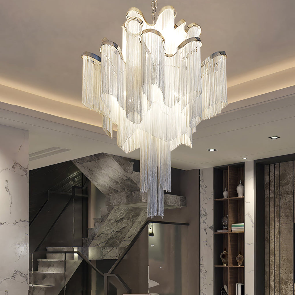 A silver Clérachic chandelier hangs lit above a marble-walled staircase, its tiers glowing warmly in the stairwell.