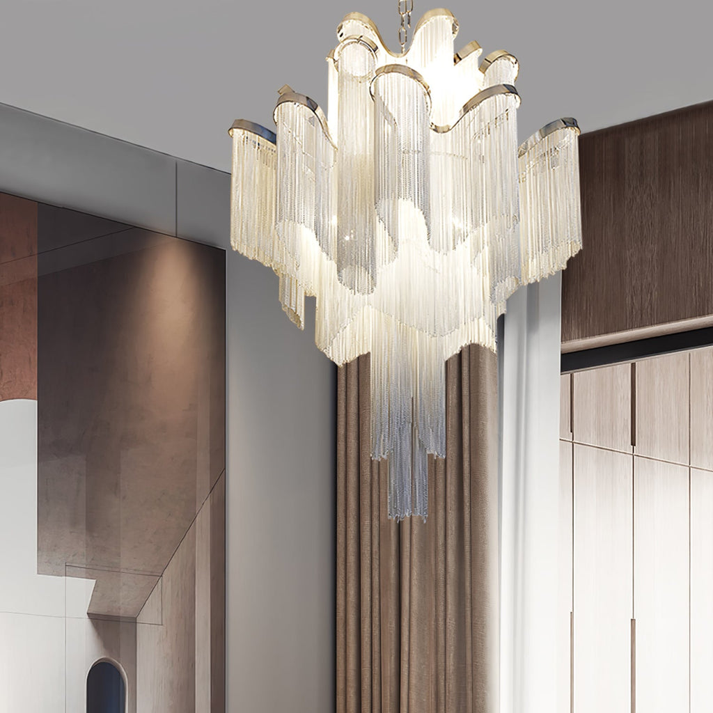Lit and tiered, this silver Clérachic chandelier hangs near a wooden staircase in a warm-toned hallway.