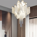 Lit and tiered, this silver Clérachic chandelier hangs near a wooden staircase in a warm-toned hallway.