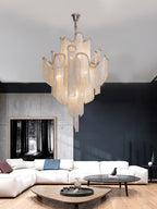 A white sofa and black side table sit beneath this lit gold Clérachic chandelier in a bright living room.
