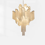 This gold Clérachic chandelier, lit, is shown against a white backdrop with its full tiered chain fringe.