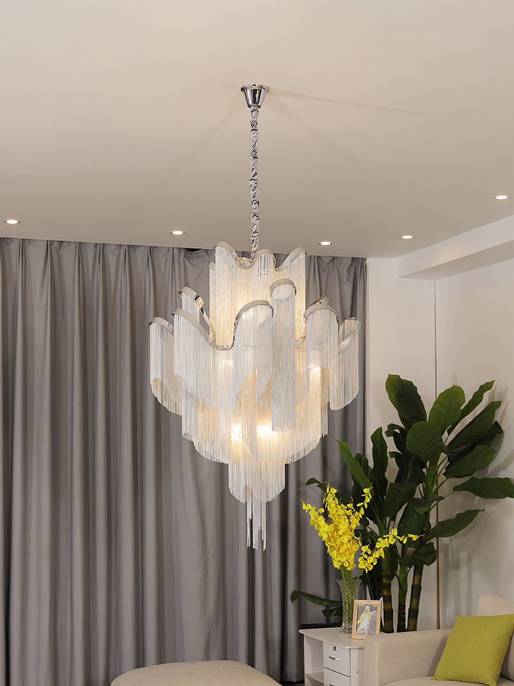 Cropped close, this lit silver Clérachic chandelier shows the full drop of its chain against grey curtains.