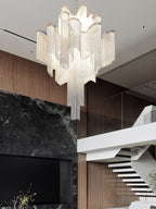 Near a dark marble fireplace and pale wooden staircase, this lit silver Clérachic chandelier hangs overhead.