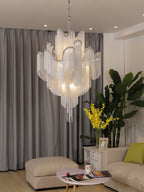 An ottoman stacked with magazines and yellow flowers sits beneath this lit silver Clérachic chandelier.