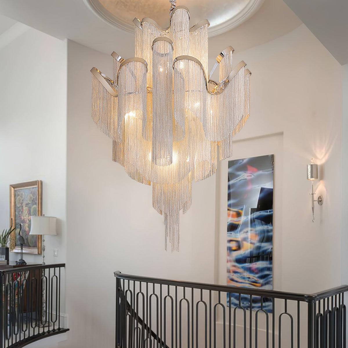 This silver Clérachic chandelier lights a white stairwell landing, with framed art and a wall sconce nearby.