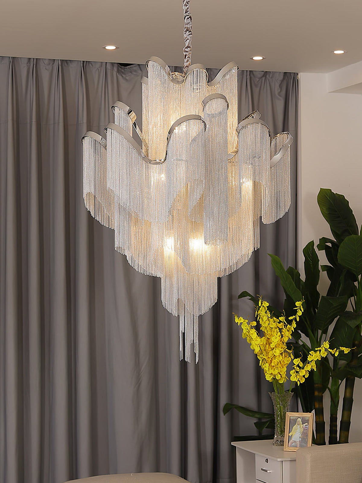 A framed photo and grey curtains sit behind this lit silver Clérachic chandelier in a living room.
