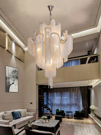 A spiral staircase and dark sofa sit beneath this lit silver Clérachic chandelier in a loft-style living room.