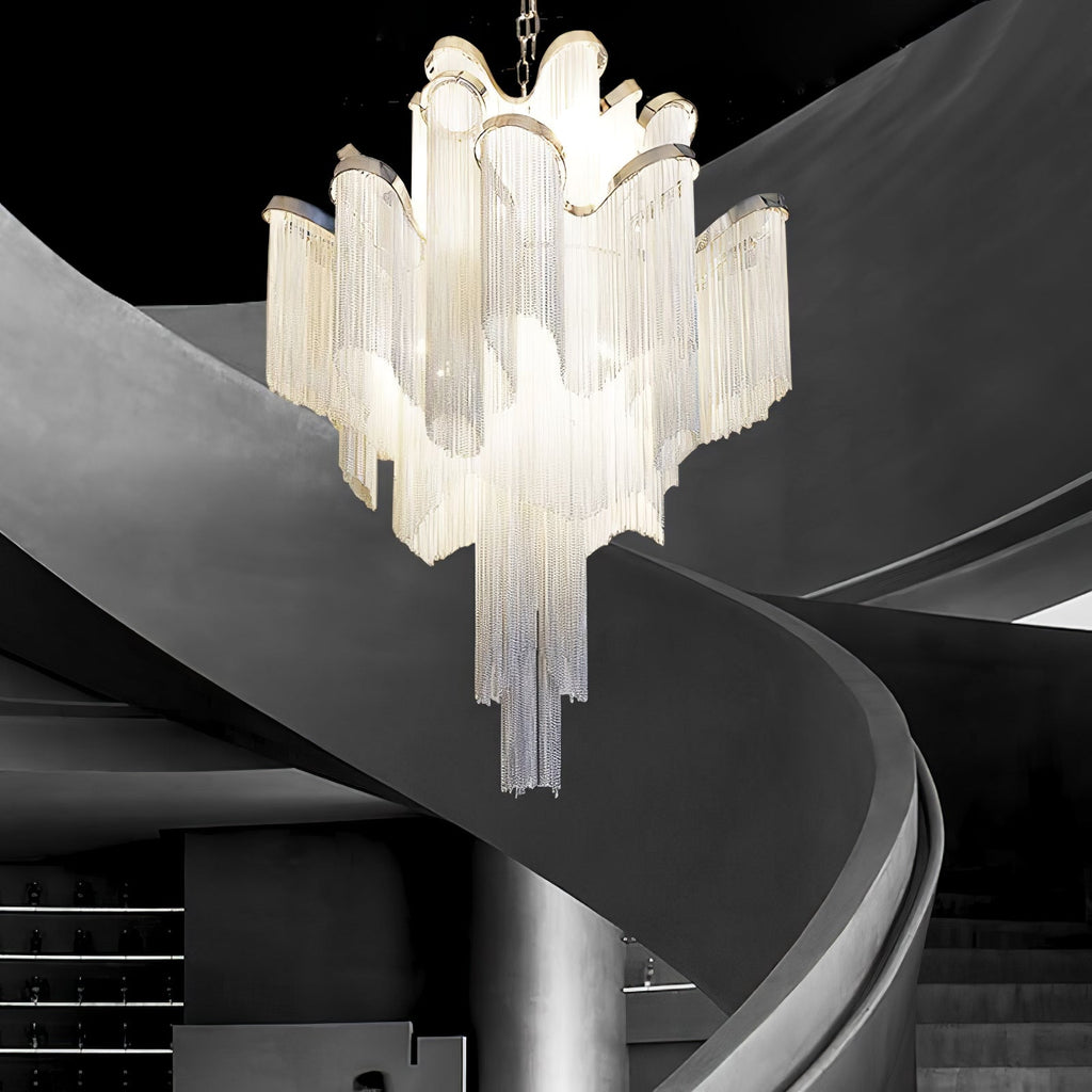This silver Clérachic chandelier hangs close beside a curved dark grey spiral staircase, lit from within.