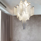 A textured taupe wall and sheer curtains frame this lit gold Clérachic chandelier in a quiet corner.