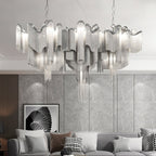 This wide silver Clérachic chandelier, lit, spans a grey panelled wall above a white sofa and patterned cushions.