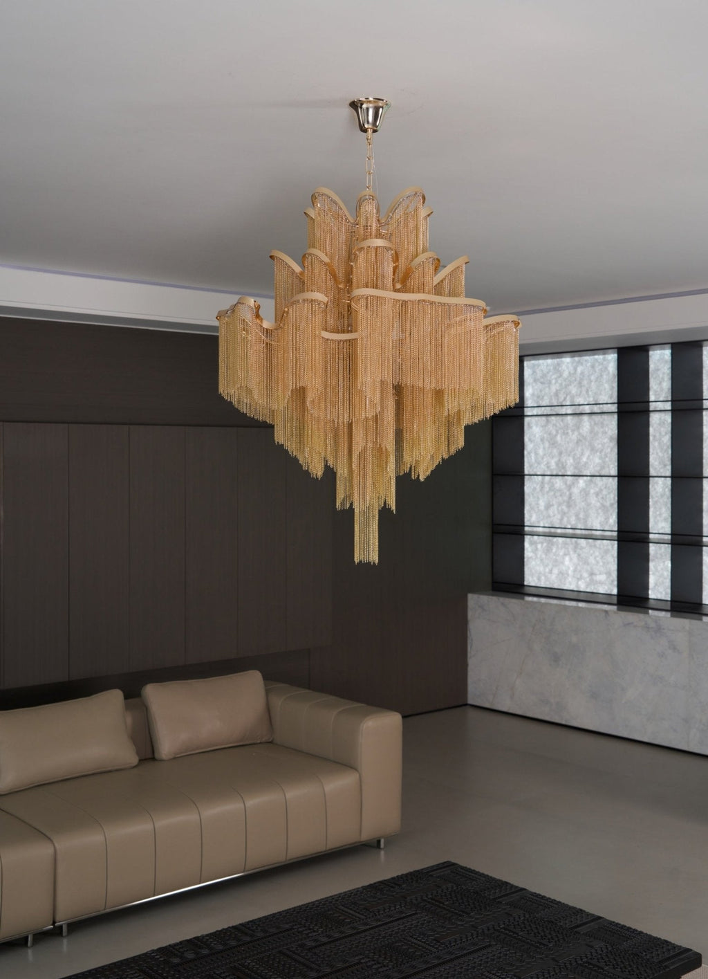 A tan leather sofa sits beneath this lit gold Clérachic chandelier in a dark living room.