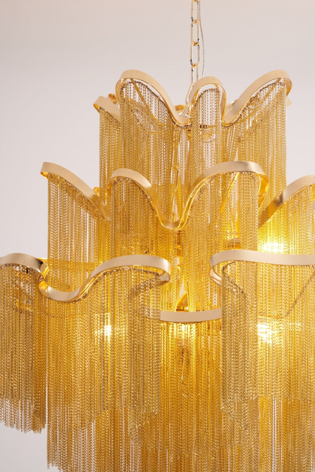 A closer view of this lit gold Clérachic chandelier shows its curved tiers and dense chain fringe.