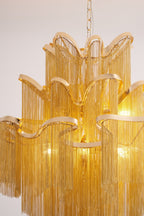 A closer view of this lit gold Clérachic chandelier shows its curved tiers and dense chain fringe.