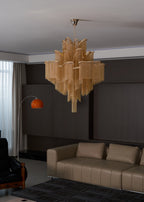 Seen from a distance, this lit gold Clérachic chandelier hangs in a lounge with tan sofas along the wall.