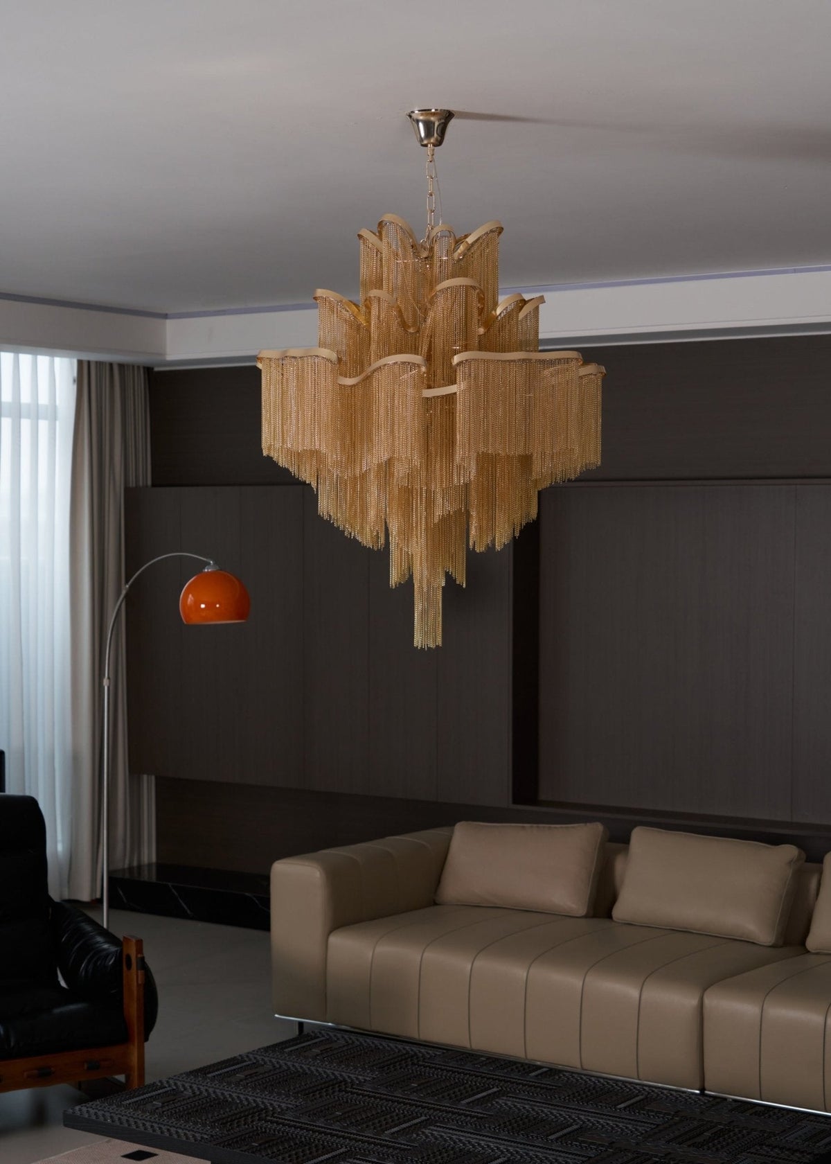Seen from a distance, this lit gold Clérachic chandelier hangs in a lounge with tan sofas along the wall.