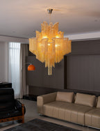 This gold Clérachic chandelier lights a living room with tan leather sofas and an orange arc floor lamp.