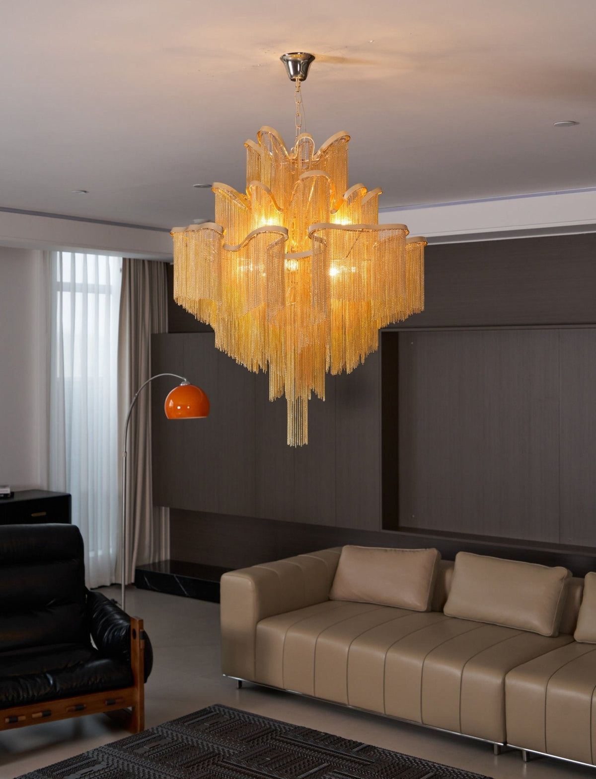 This gold Clérachic chandelier lights a living room with tan leather sofas and an orange arc floor lamp.