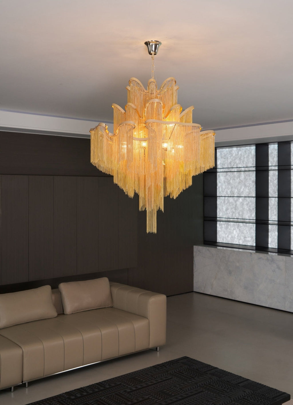Above a tan leather sofa in a dark wood-panelled lounge, this lit gold Clérachic chandelier hangs overhead.