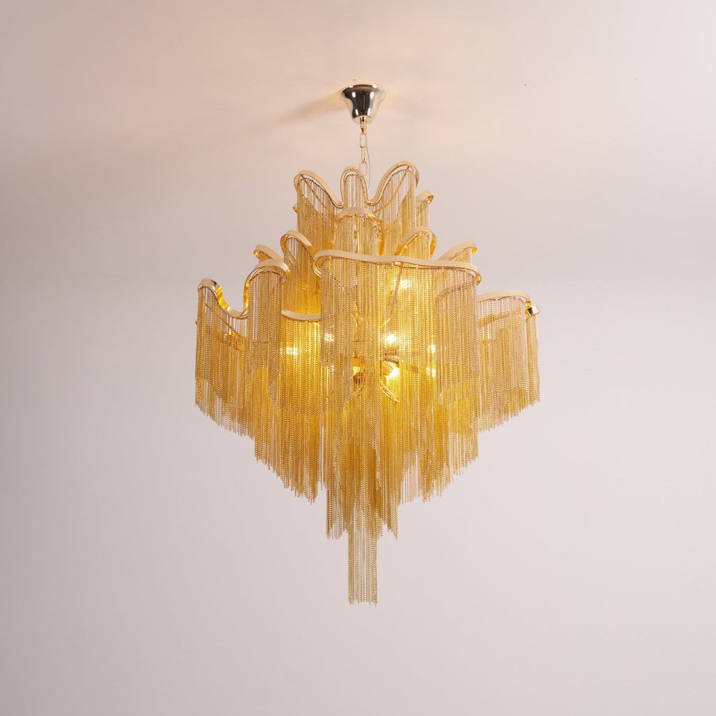 On a plain backdrop, this lit gold Clérachic chandelier shows its ceiling mount plate above the tiers.