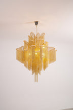A gold Clérachic chandelier, unlit, is shown against a white backdrop with its chain hanging in tiers.