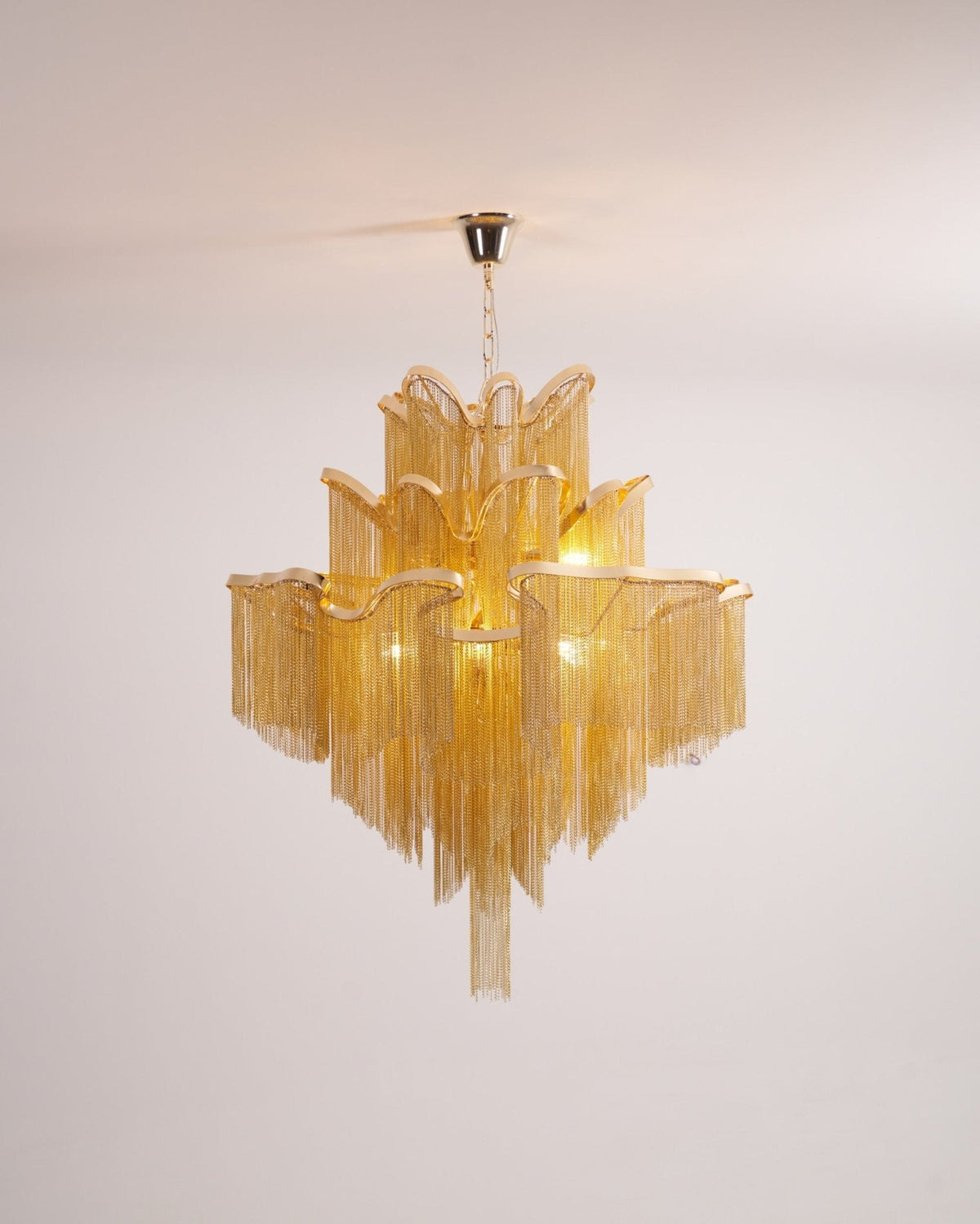 Fully spread on a white backdrop, this lit gold Clérachic chandelier shows its tiered chain fringe.