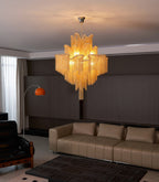 A gold Clérachic chandelier lights a lounge with tan leather sofas and an orange arc floor lamp.