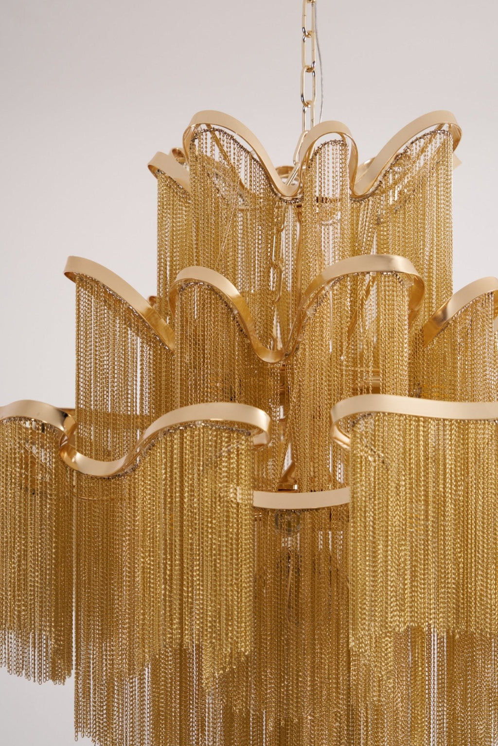 Close view of the wide arched tiers and chain fringe on this lit gold Clérachic chandelier.