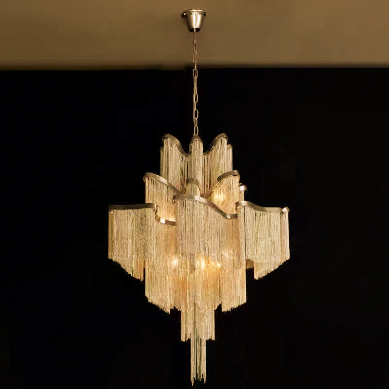 A gold Clérachic chandelier glows against a plain black backdrop, its tiers lit from within.