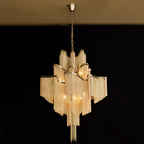 A gold Clérachic chandelier glows against a plain black backdrop, its tiers lit from within.