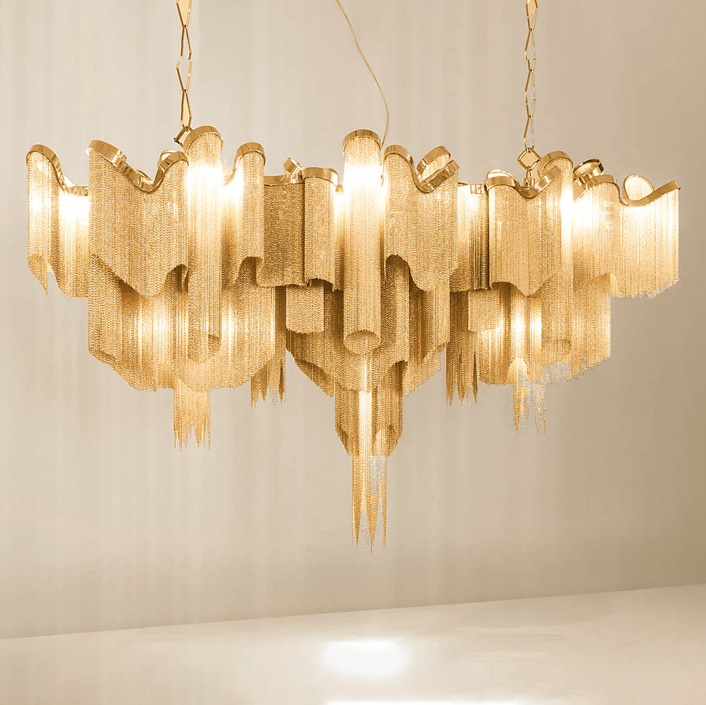 This wide gold Clérachic chandelier, lit, is shown on a plain backdrop with its chain spread outward.