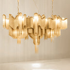 This wide gold Clérachic chandelier, lit, is shown on a plain backdrop with its chain spread outward.