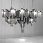 Several tiers of this silver Clérachic chandelier cluster together, lit, against a plain grey backdrop.