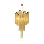 Trailing to a point, this lit gold Clérachic chandelier is shown against a white backdrop.