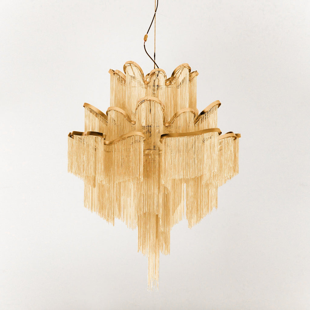 This gold Clérachic chandelier is shown unlit against a cream backdrop, its tiers fully spread.