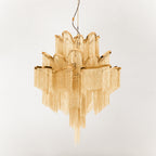 This gold Clérachic chandelier is shown unlit against a cream backdrop, its tiers fully spread.